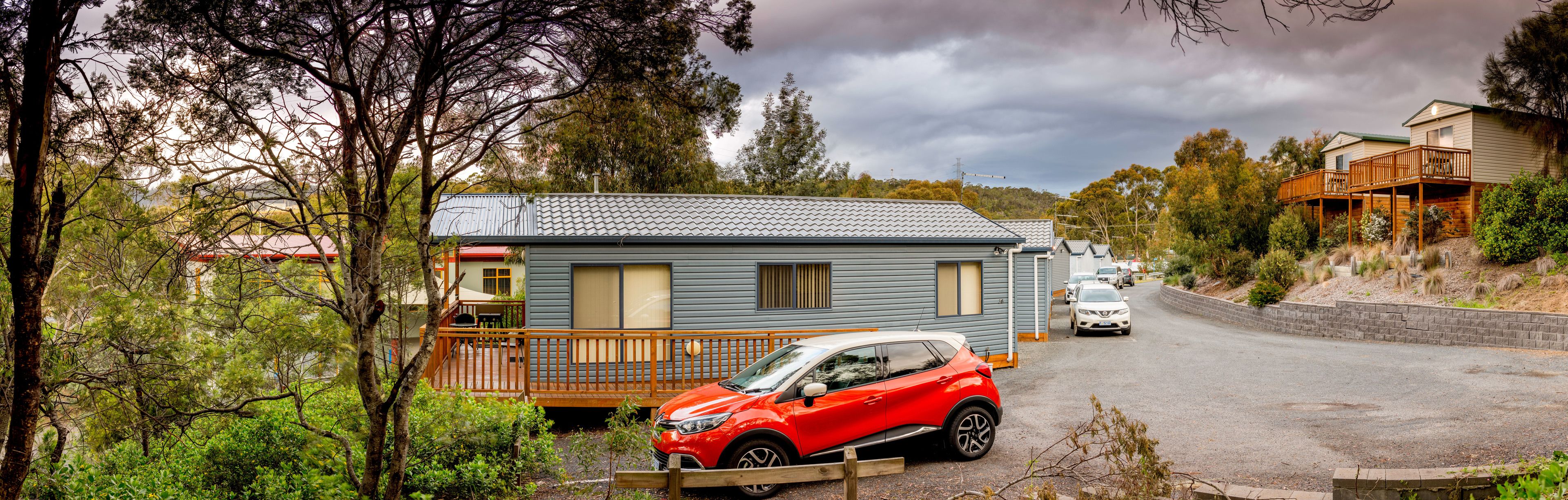 A mobile home with a wooden deck and a car parked in front.