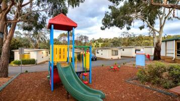 Children can play on the green slide, climb the colorful structure, and explore the playhouse in this outdoor playground surrounded by trees.