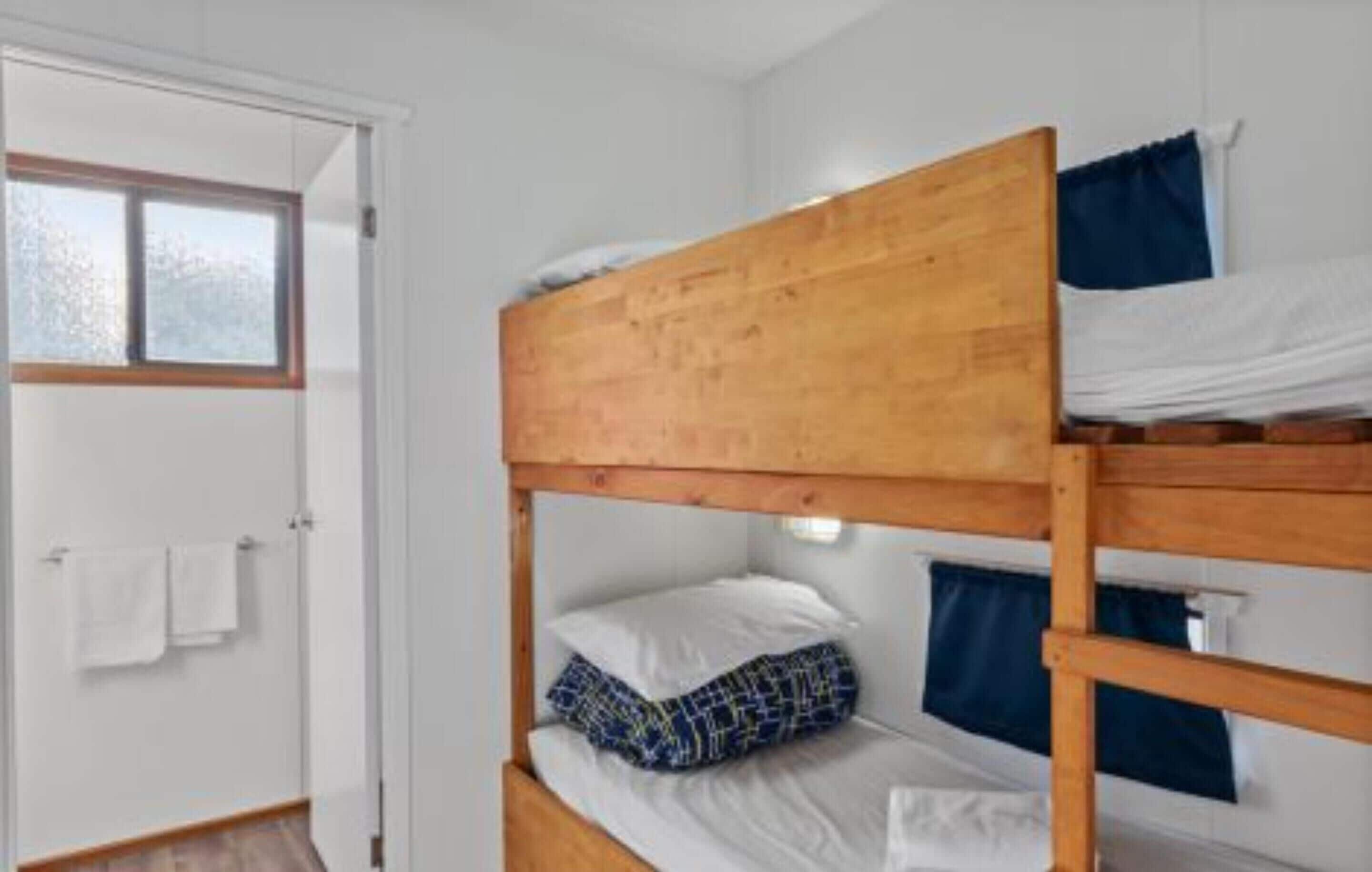 A bunk bed room with a wooden headboard, white bedding, and a window with a view.