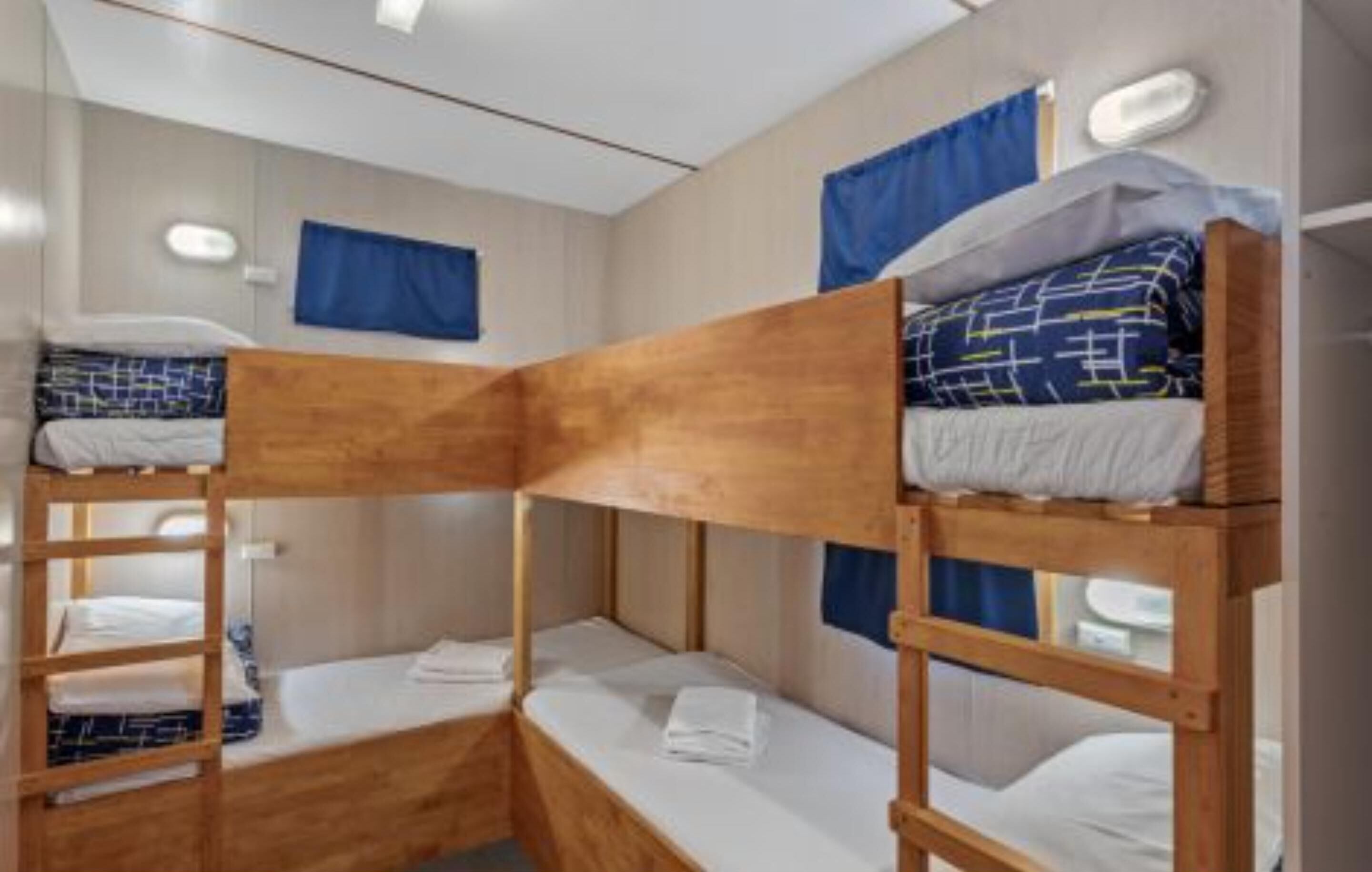 Habitación con literas de madera, ropa de cama blanca y cortinas azules.