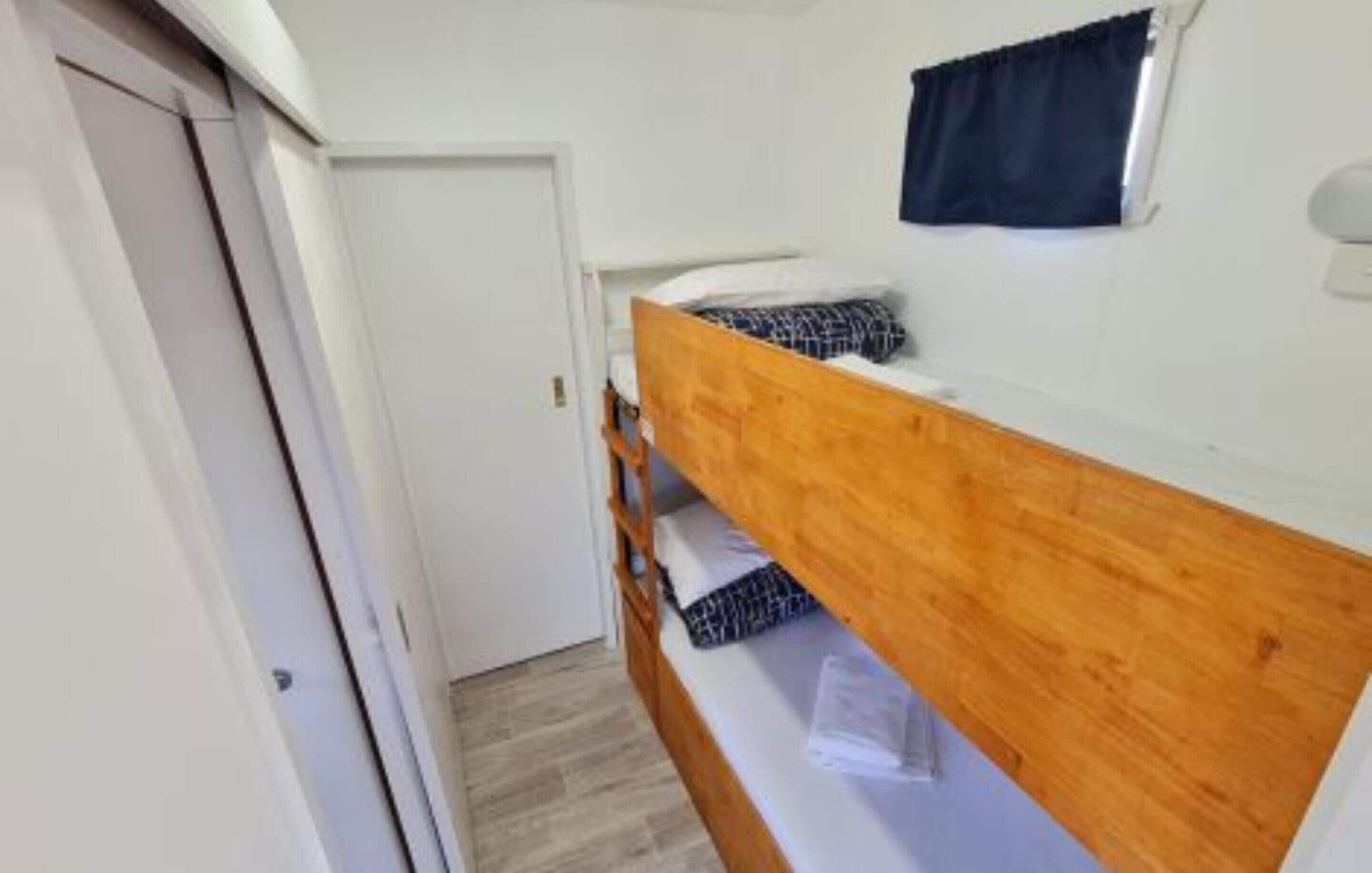 A single bunk bed room with a wooden headboard, a small window with dark curtains, and a white door.