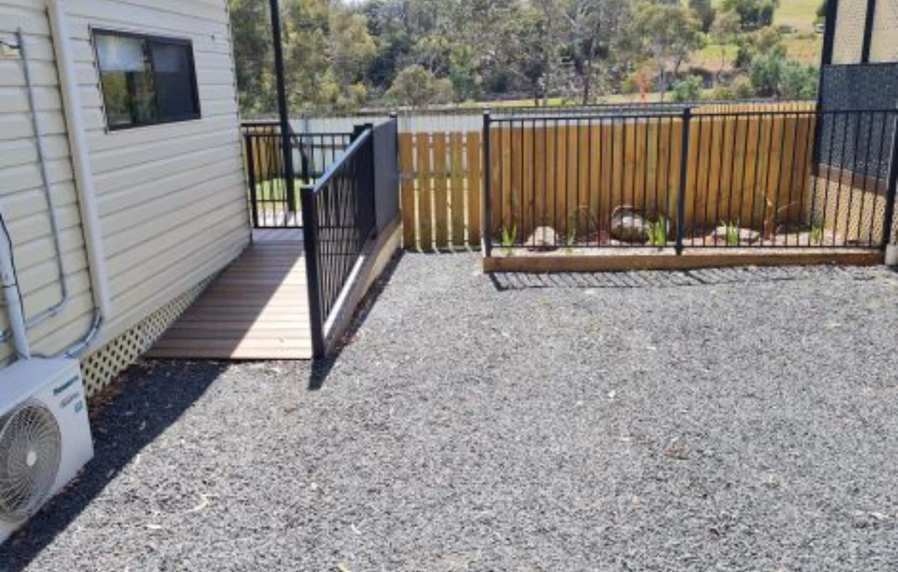 A covered outdoor area with a gravel floor, a wooden deck, and a metal fence.