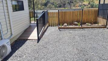 A covered outdoor area with a gravel floor, a wooden deck, and a metal fence.