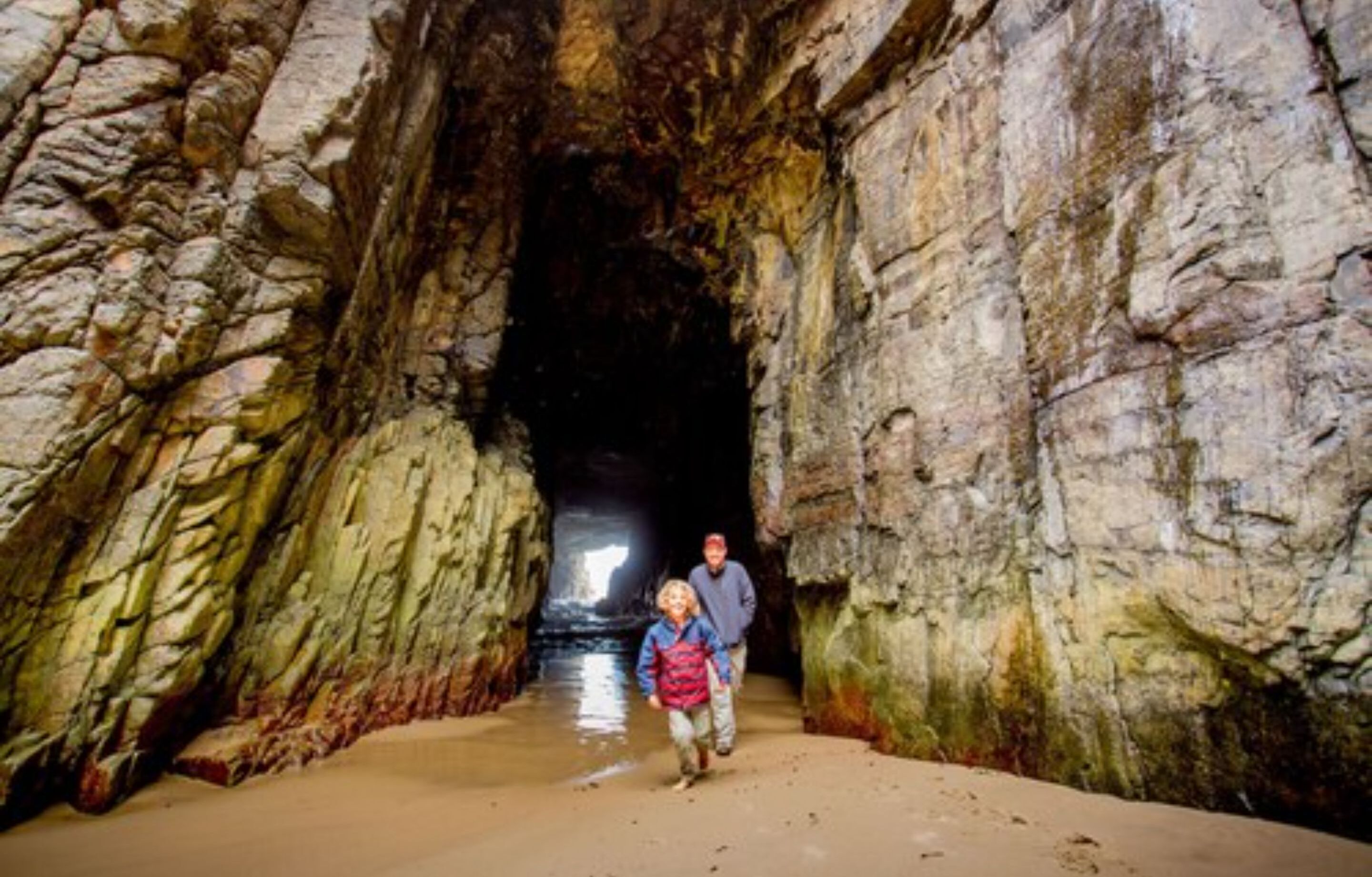 Um estreito corredor de caverna com paredes rochosas e chão arenoso.