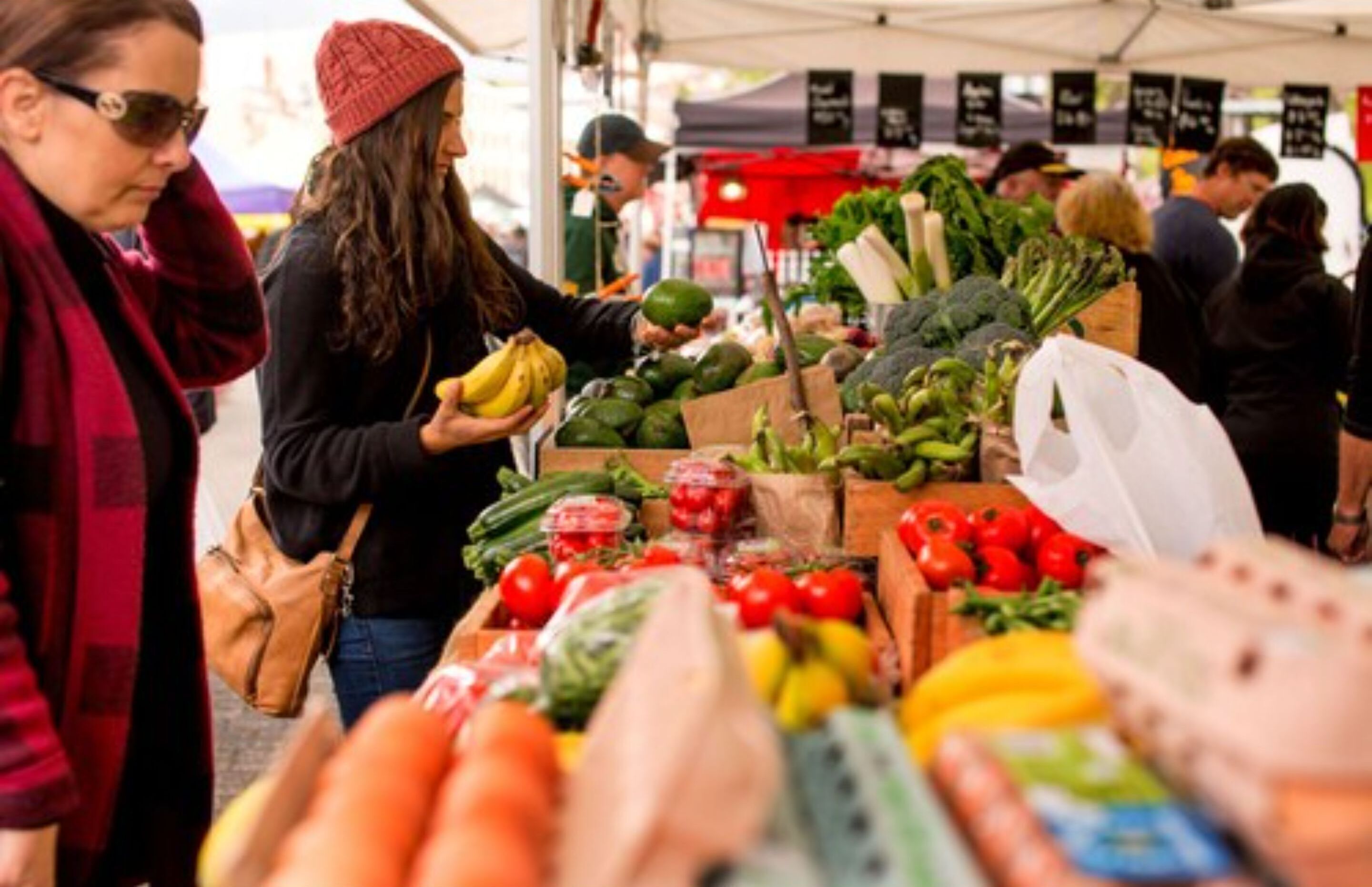 Un étal de marché proposant des produits frais, notamment des tomates, des poivrons et des légumes-feuilles.