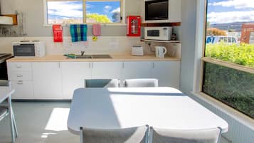 A compact kitchen with a microwave, toaster, and sink. There is a table and chairs, and a window with a view of greenery and buildings.