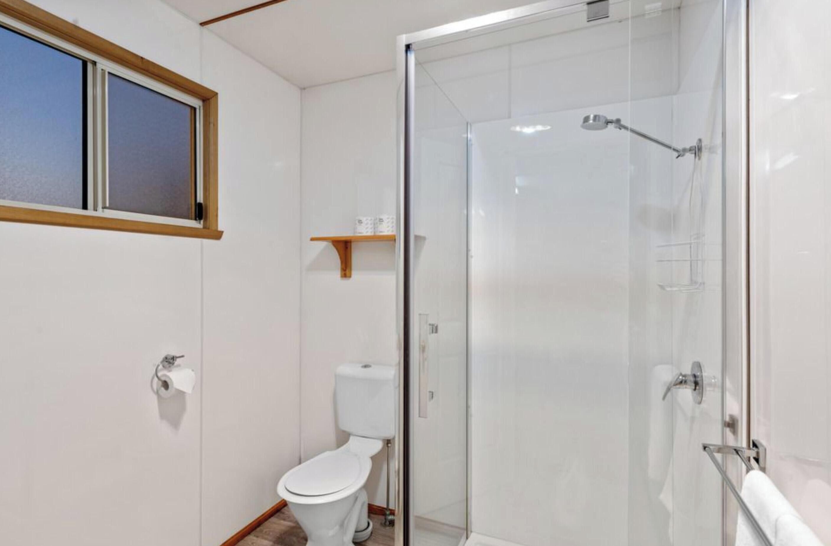Un baño con inodoro, cabina de ducha de vidrio y ventana con persianas.