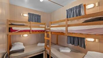 Une chambre avec un lit superposé, comportant deux lits, chacun avec un oreiller et une couverture. Une échelle relie les deux lits, et la chambre est équipée d’un luminaire fixé au mur.
