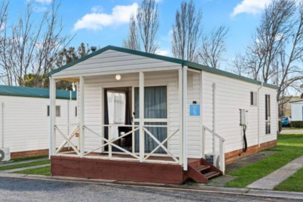 A single-story mobile home with a porch, a small front yard, and a clear sky.