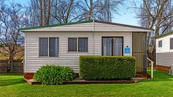 A single-story mobile home with a green roof, a small front yard with a hedge, and a blue handicap parking sign.