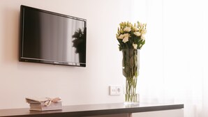 Un televisor de pantalla plana montado en una pared, un florero con flores sobre una mesa y una pila de libros con una cinta.