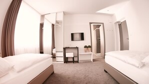 Habitación de hotel con dos camas, un escritorio, un televisor y zona de ducha.