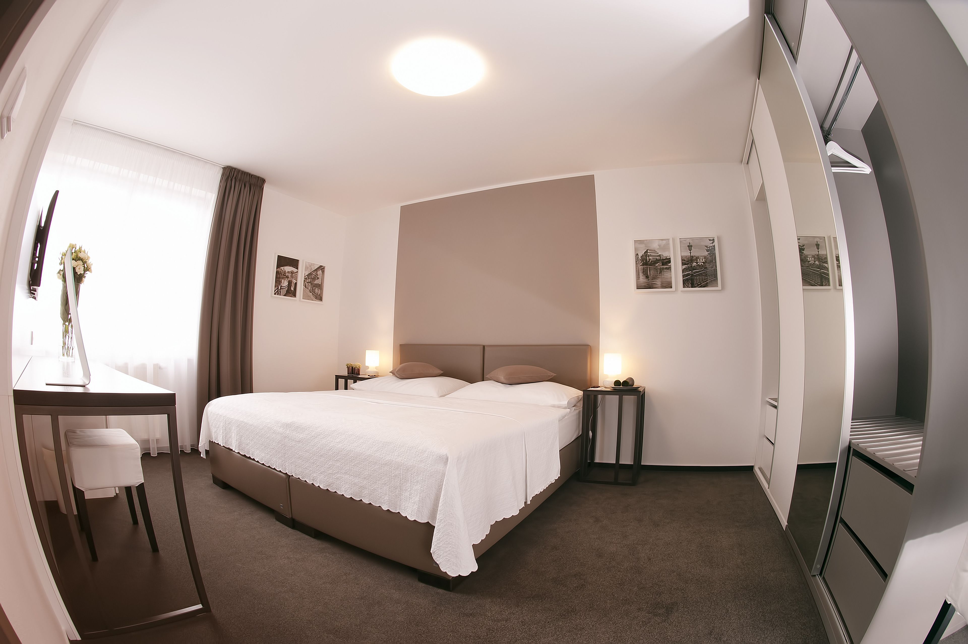Ein ordentlich eingerichtetes Hotelzimmer mit einem großen Bett, Nachttischen, einem Schreibtisch und einem Sessel.