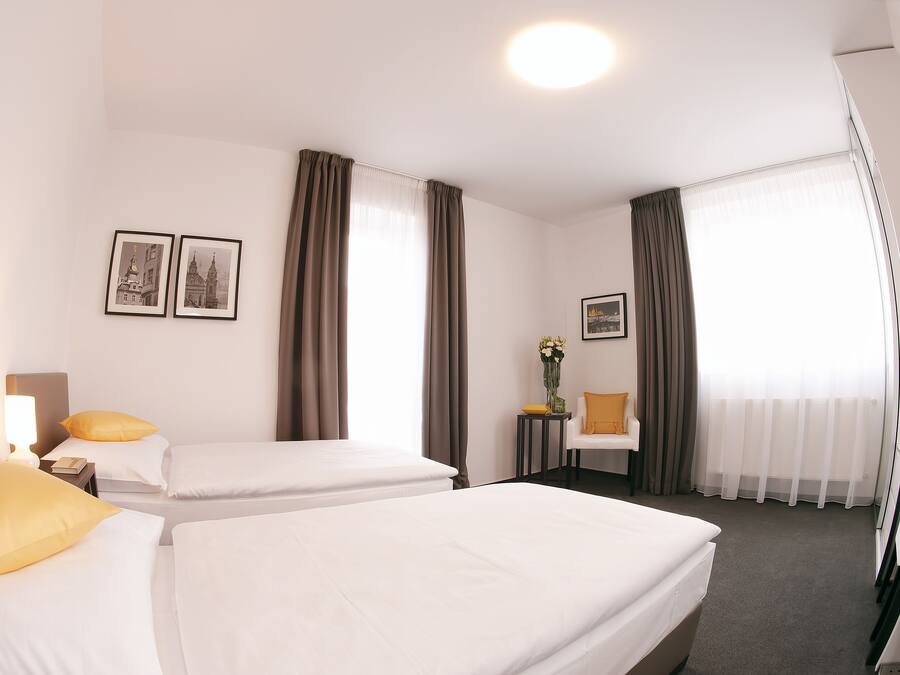 Une chambre d’hôtel avec deux lits simples, un bureau, une chaise, une petite table avec un vase et deux tableaux encadrés au mur.