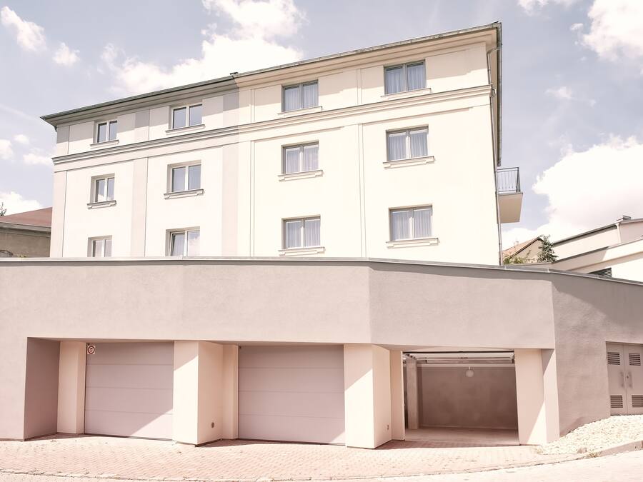 Un edificio de varios pisos con fachada plana, varias ventanas y una zona de estacionamiento techada.