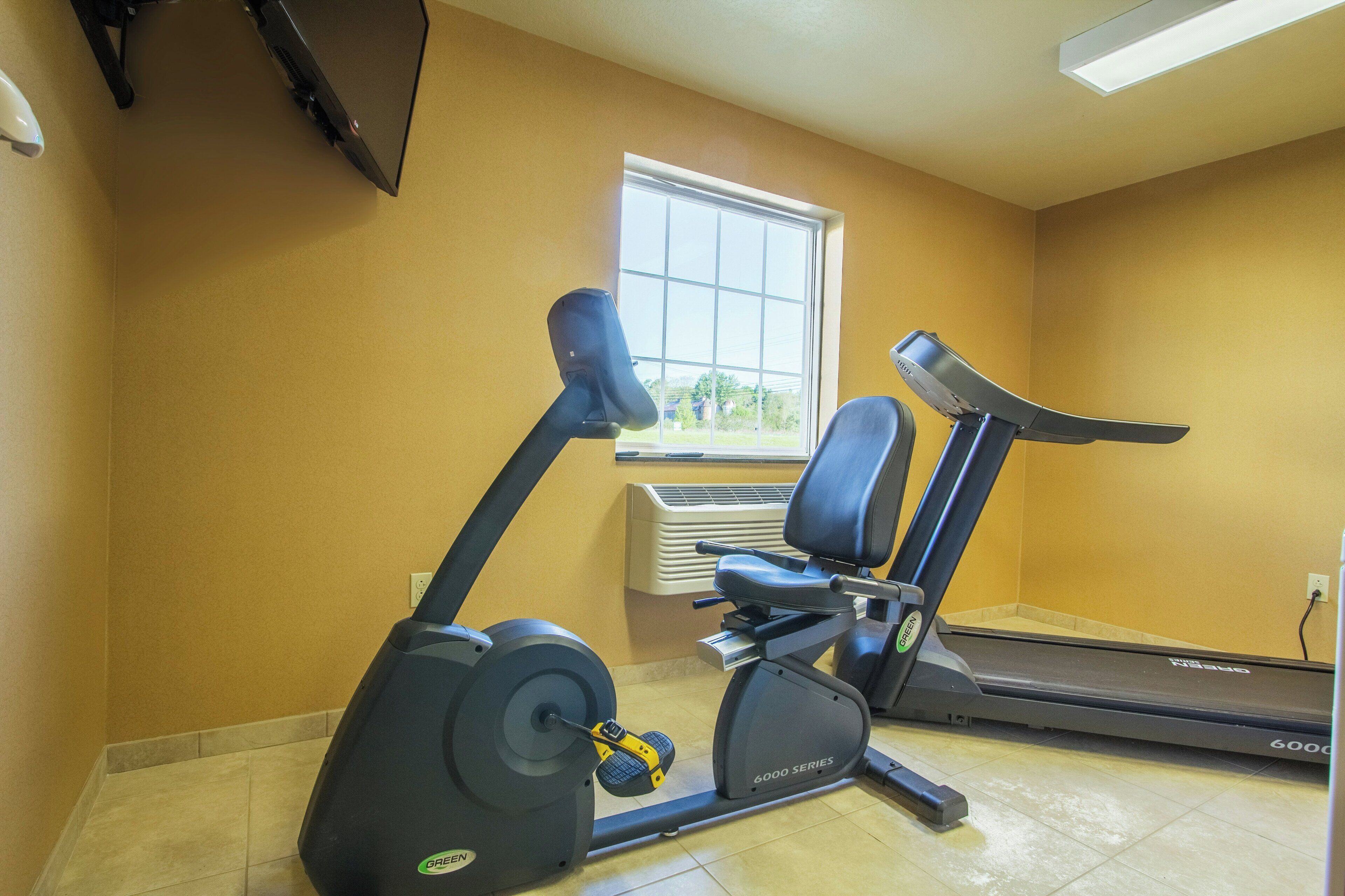 Une salle de sport équipée de matériel d’exercice, avec une fenêtre et un climatiseur fixé au mur.