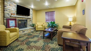 A living room with a stone fireplace, a flat-screen TV, a sofa, a chair, a coffee table, and a patterned carpet.