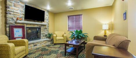 A living room with a stone fireplace, a flat-screen TV, a sofa, a chair, a coffee table, and a patterned carpet.