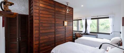 Een slaapkamer met twee bedden, houten lambrisering, een plafondventilator en een raam met gordijnen.