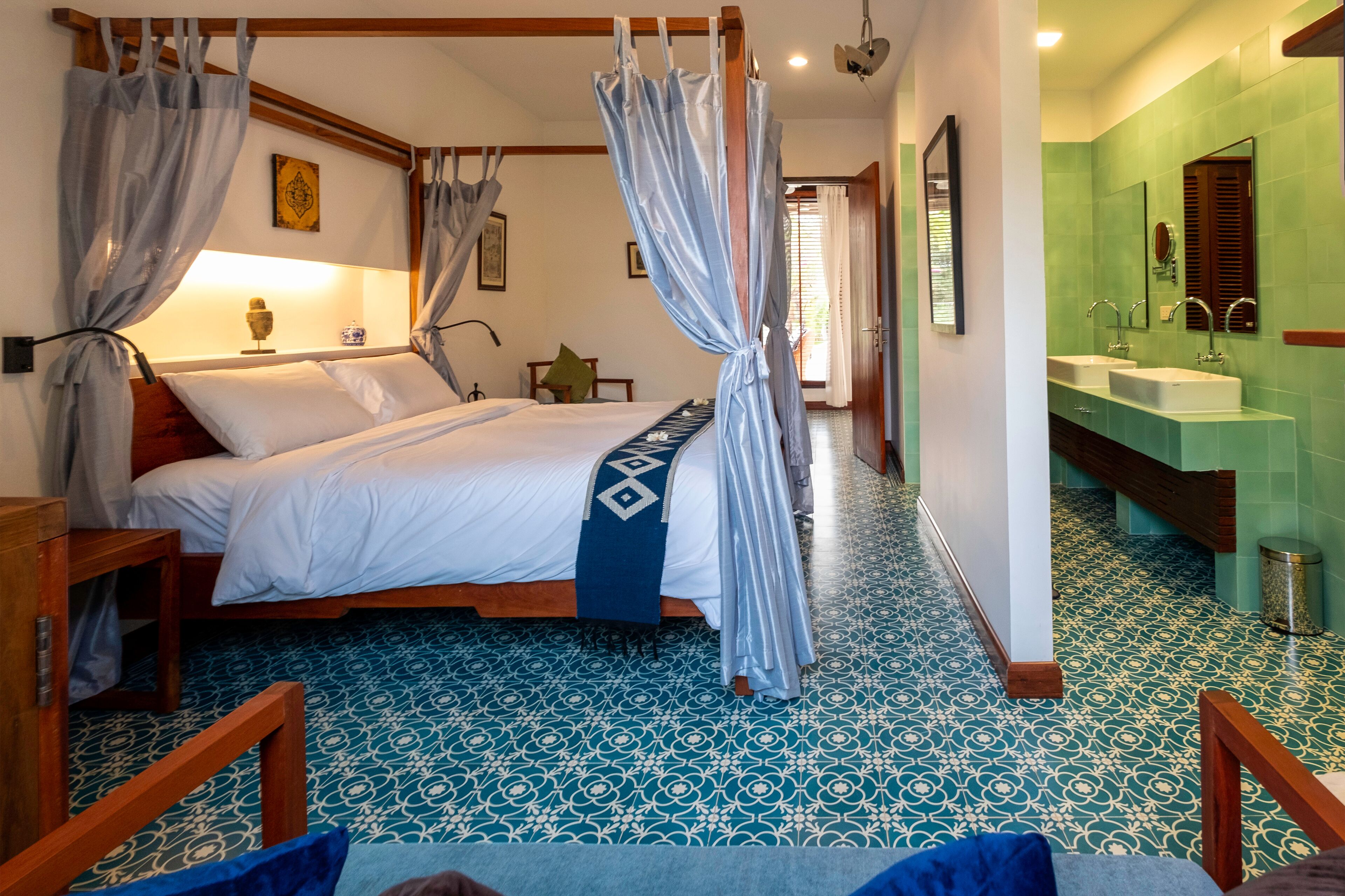 Un dormitorio con cama con dosel, mesita de noche, lámpara decorativa y estante en la pared.