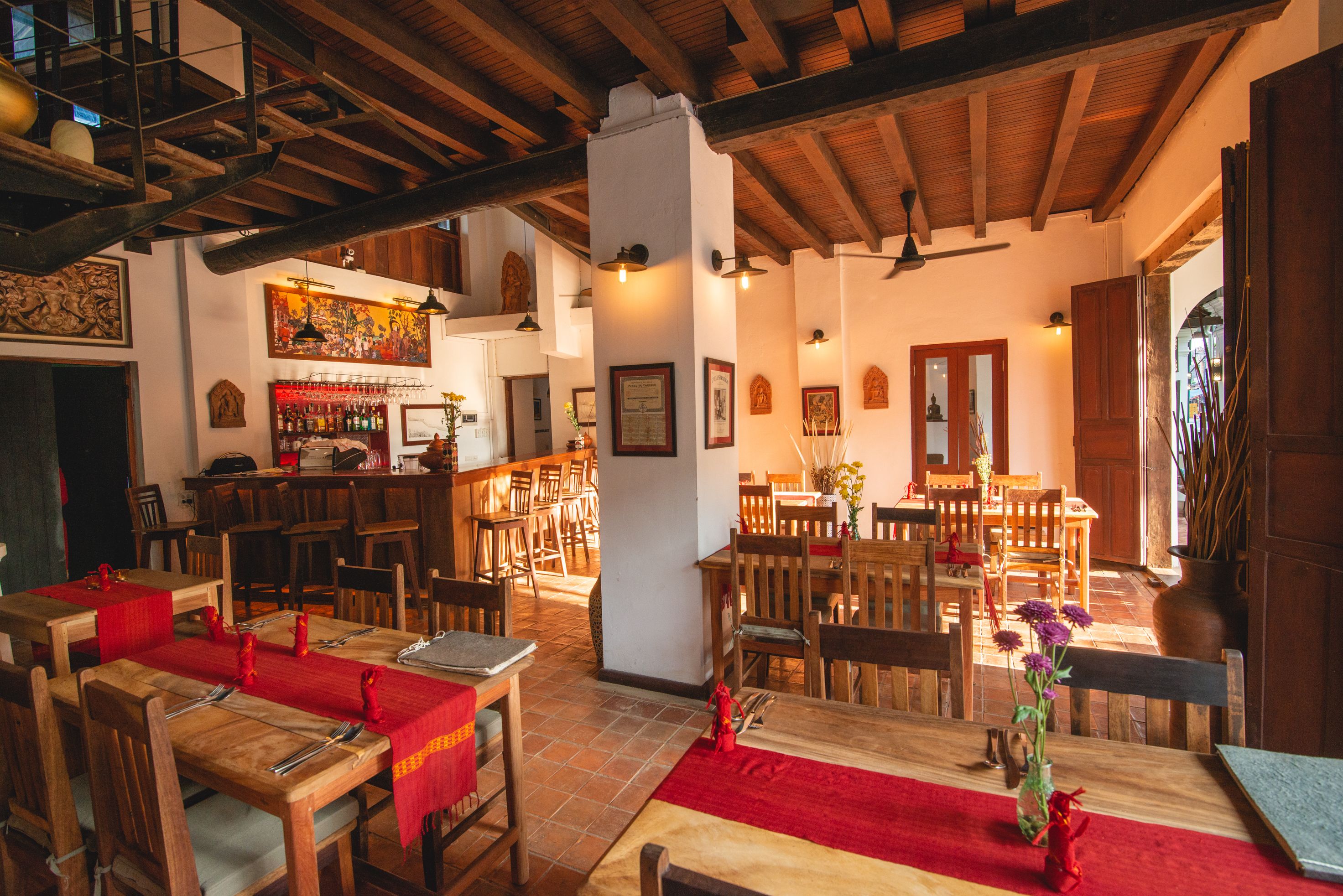 Un restaurante con mesas y sillas de madera, una zona de bar y un techo alto con vigas a la vista.
