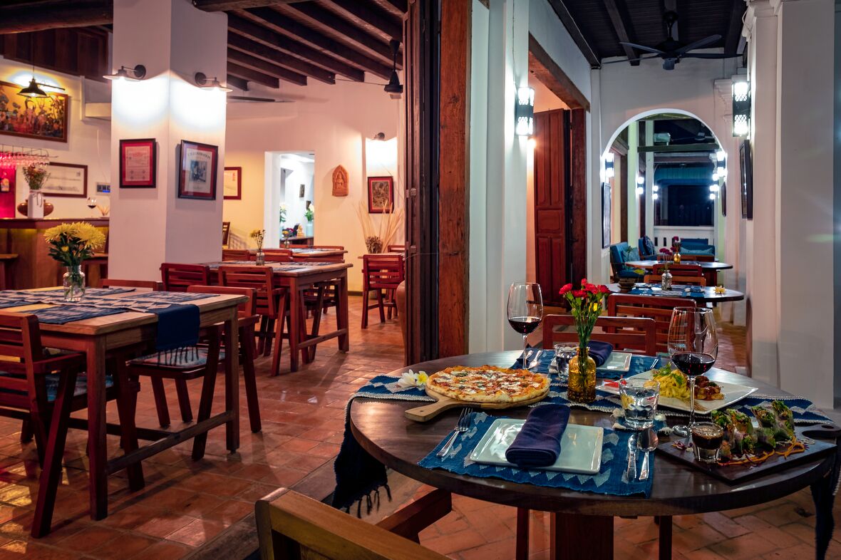 A restaurant with wooden tables and chairs, a pizza on one table, and a wine glass on another.