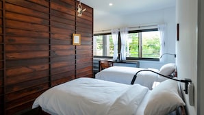 Een hotelkamer met twee bedden, houten lambrisering aan een muur, een raam met gordijnen en een plafondventilator.
