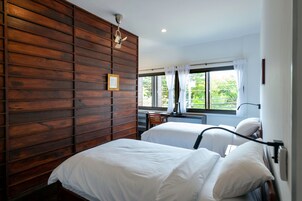 Habitación de hotel con dos camas, paneles de madera en una pared, una ventana con cortinas y un ventilador de techo.