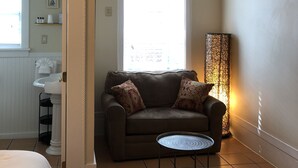A room with a ceiling fan, an air conditioning unit, a window with blinds, a sofa with patterned cushions, a small round table, and a floor lamp. - L'Habitation Guest House - Adults Only (Key West)