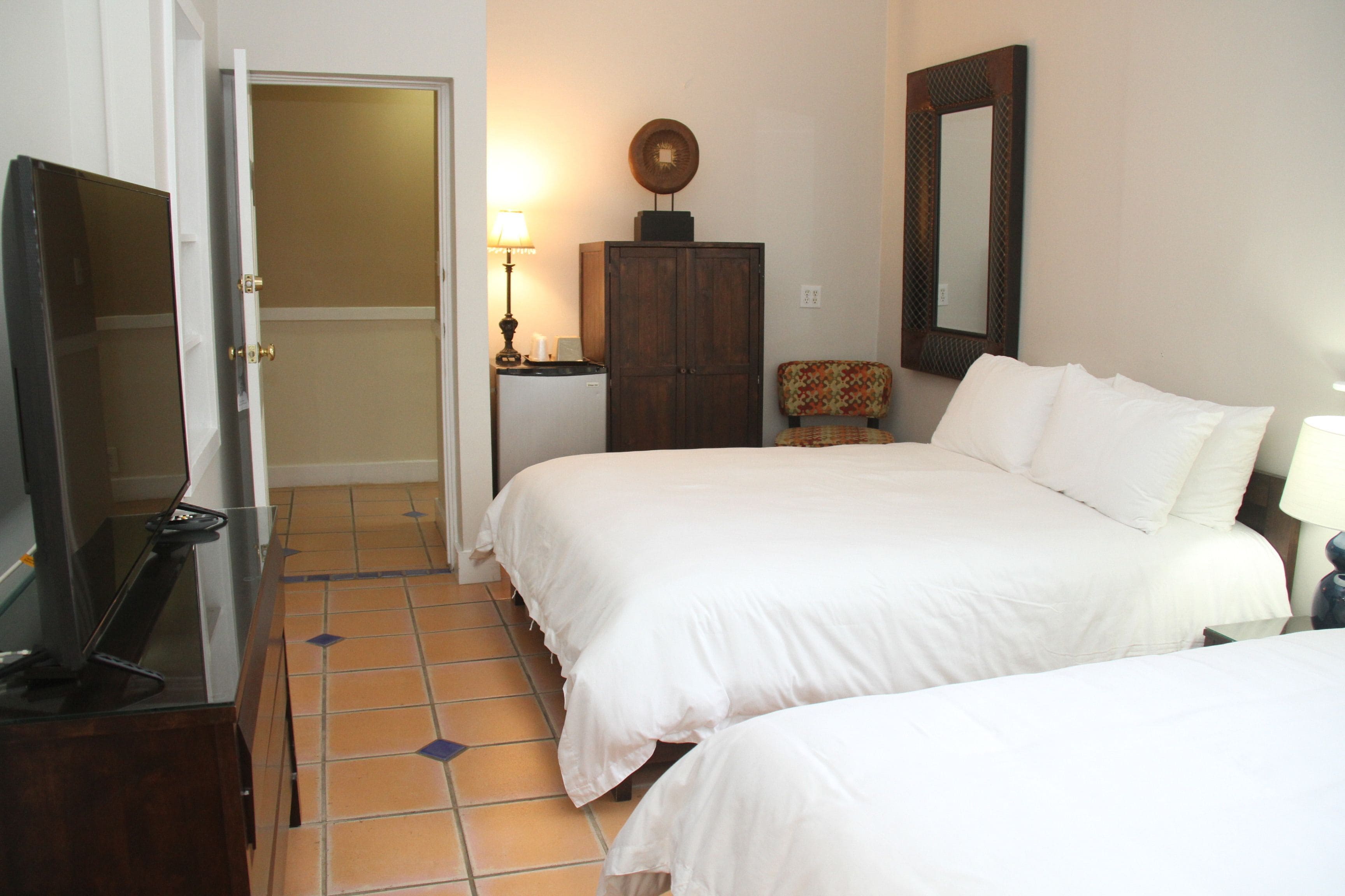 A hotel room with two beds, a wardrobe, a desk with a lamp, and a television.