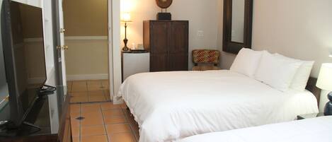 A hotel room with two beds, a wardrobe, a desk with a lamp, and a television.