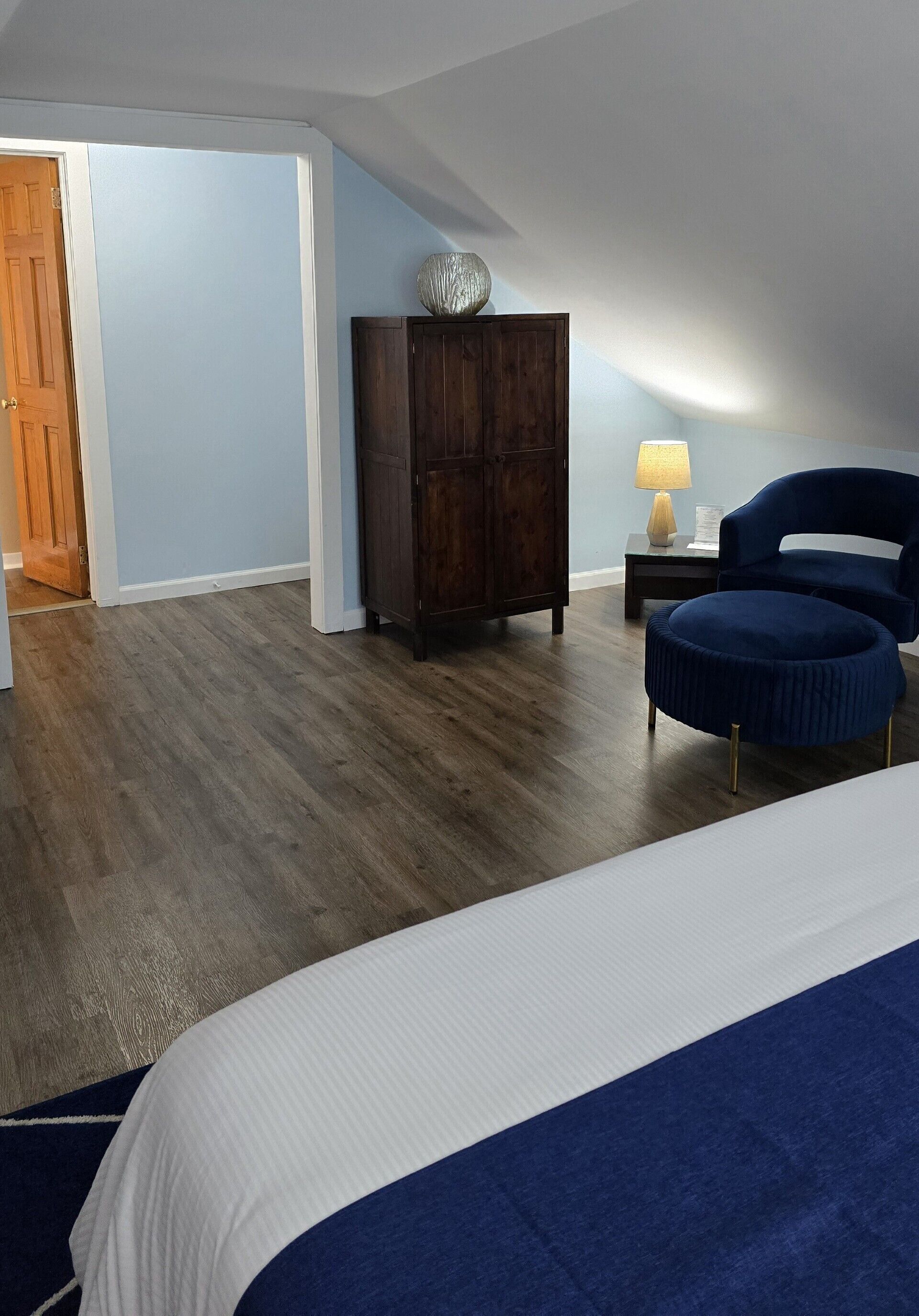 A bedroom with a bed, a wooden cabinet, a blue chair, and a nightstand with a lamp.