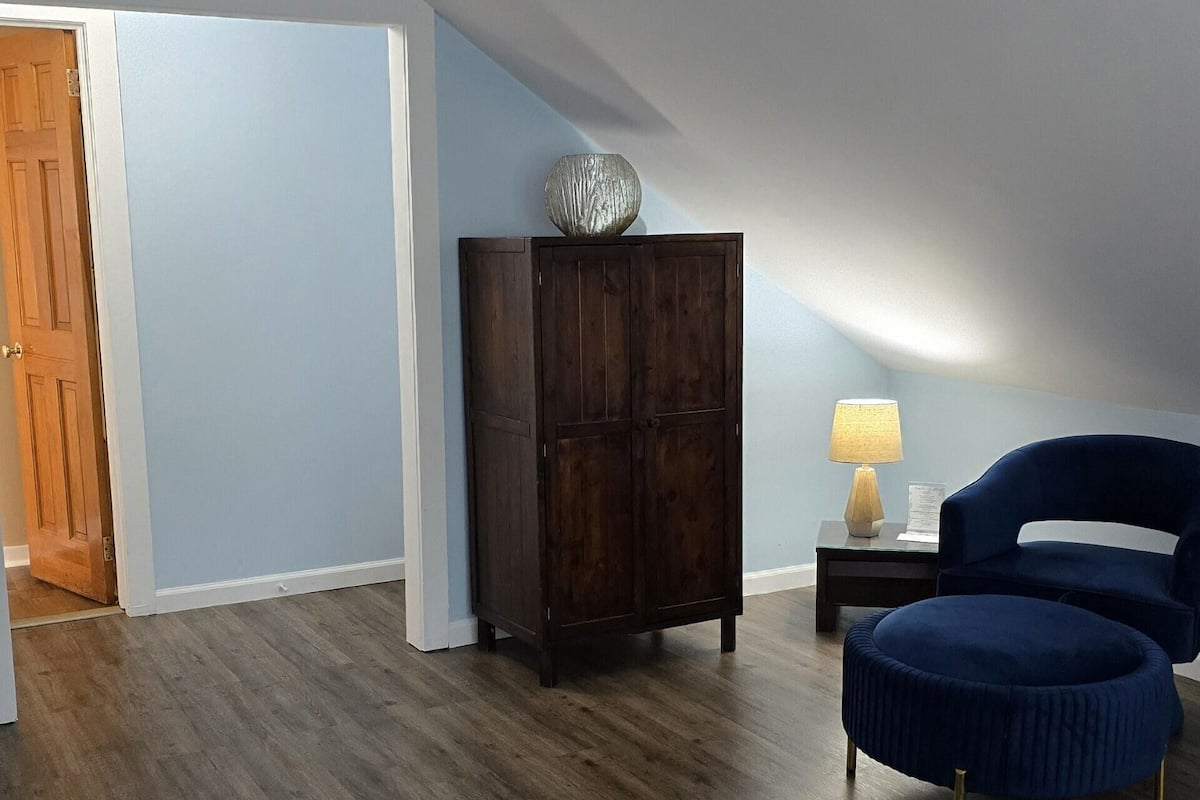 A bedroom with a bed, a wooden cabinet, a blue chair, and a nightstand with a lamp.