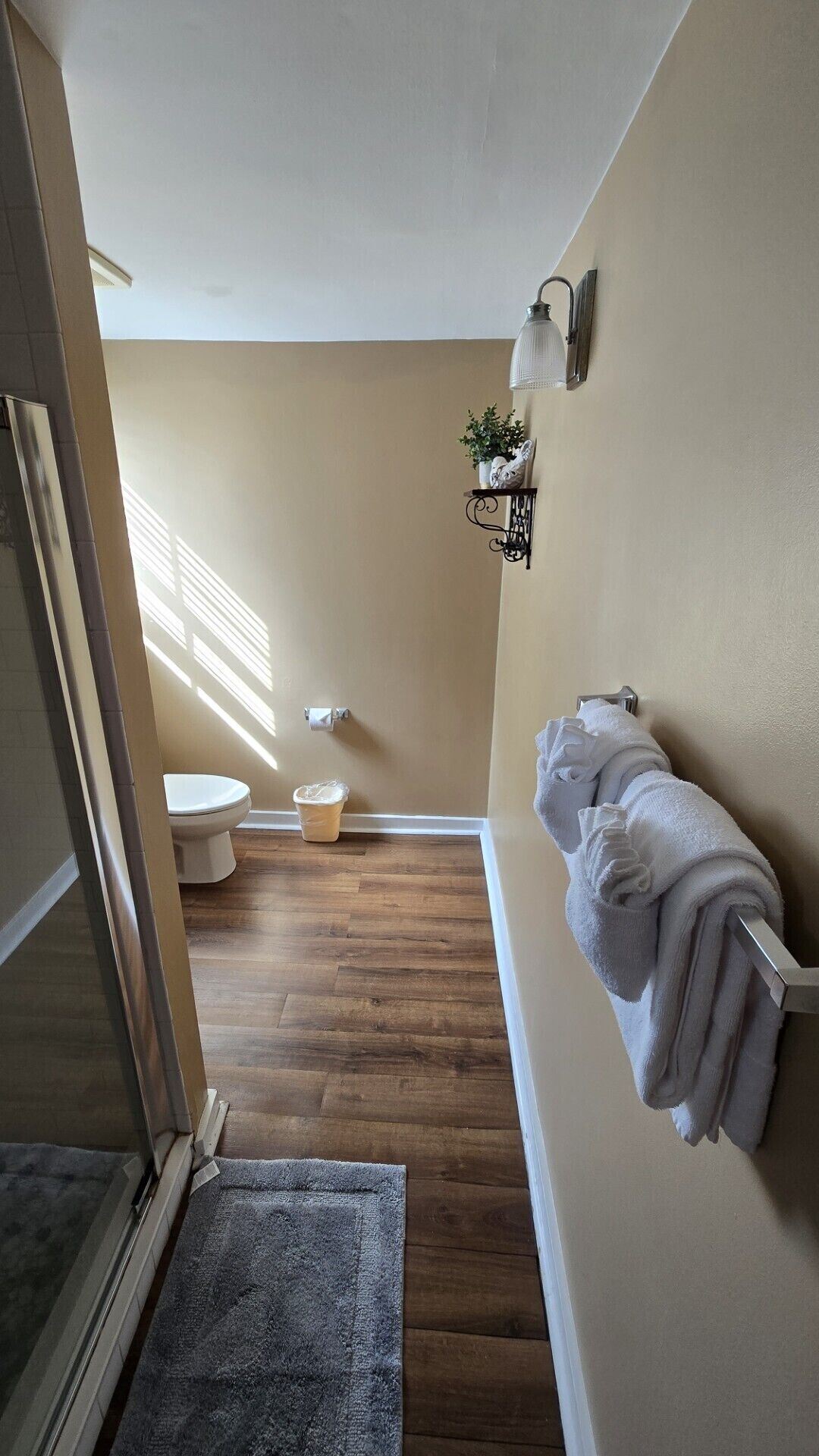 Une salle de bain comprenant des toilettes, un lavabo, un porte-serviettes et une petite étagère sur laquelle est posée une plante.