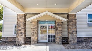 Una entrada de edificio con fachada de piedra, una puerta blanca con paneles de vidrio y un porche cubierto.