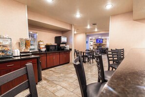 A hotel dining area with a counter, seating, and a television in the background. - Cobblestone Inn & Suites – Big Lake (Big Lake)