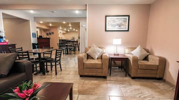 A hotel lobby with a seating area, a coffee station, and a dining area in the background.
