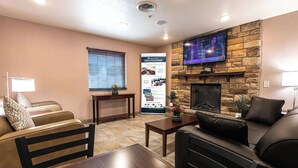Una sala de estar con chimenea de piedra, un televisor montado en la pared, un sofá, una mesa de centro y una mesita con una planta.