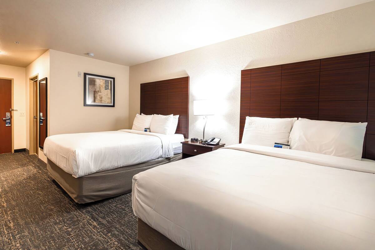 A hotel room with two beds, a wooden headboard, a framed picture on the wall, and a bedside table with a lamp.
