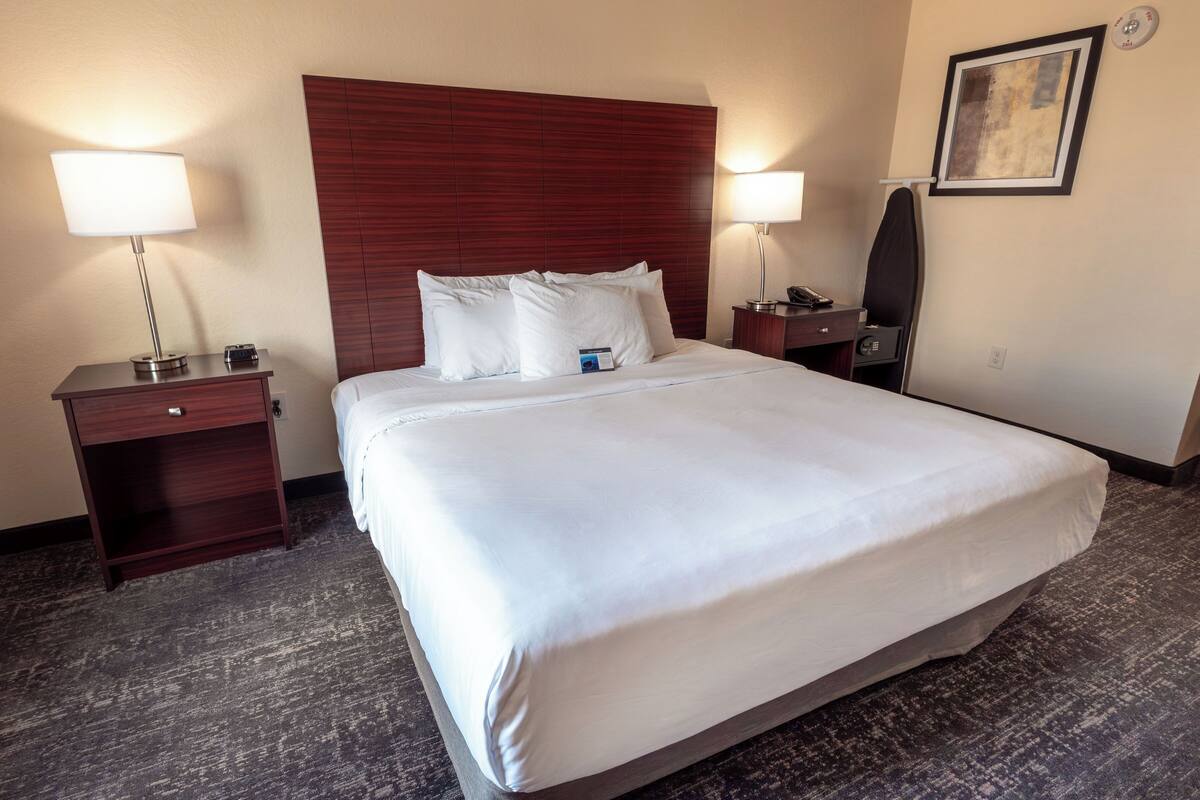 A hotel room with a large bed, two bedside tables, a nightstand, a lamp, a mirror, and a framed picture on the wall.