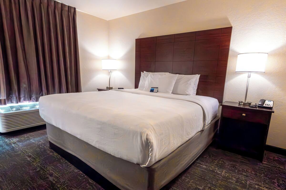 A hotel room with a large bed, two bedside lamps, a nightstand, and a wall-mounted heater.