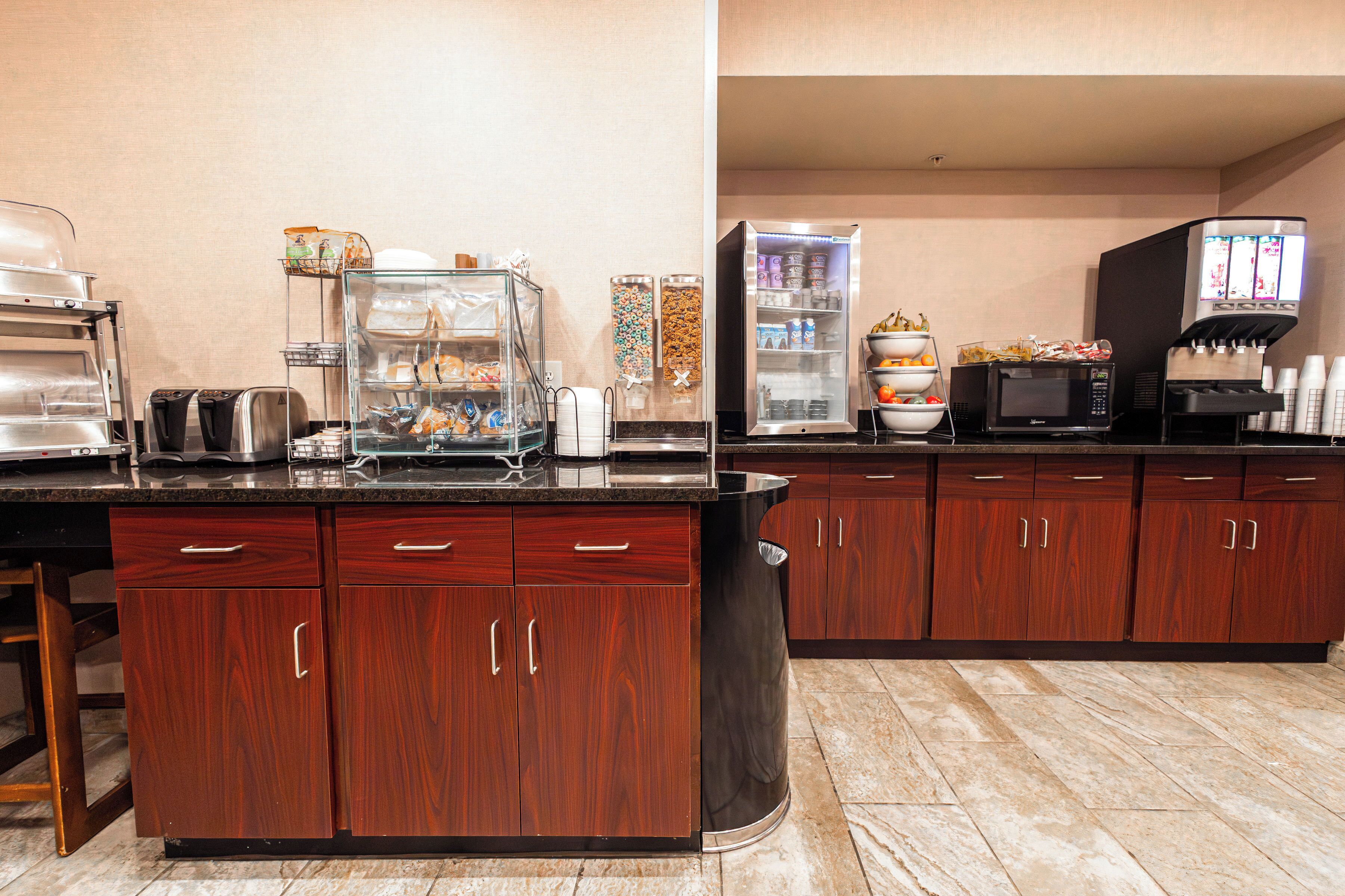 A kitchen area with a buffet setup, including a refrigerator, microwave, and various food containers.
