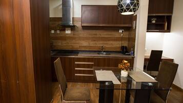 Una cocina moderna con armarios de madera, una campana extractora de acero inoxidable, una mesa de vidrio con cuatro sillas y una lámpara colgante.