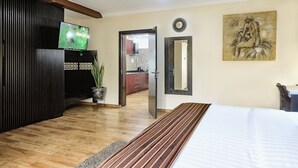 Una habitación de hotel moderna con una cama grande, un televisor de pantalla plana, piso de madera, una planta en maceta y un cuadro en la pared.