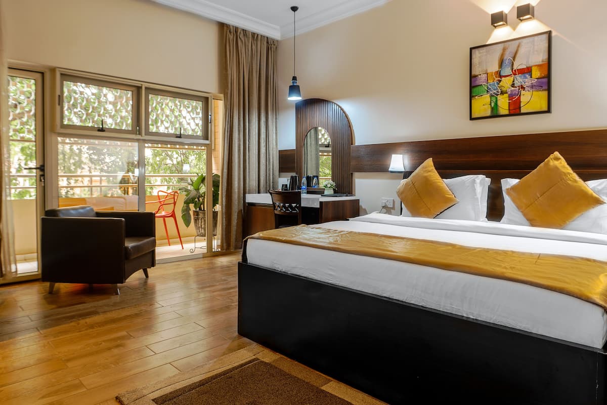 A hotel room with a large bed, a desk, a chair, and a view through a sliding door.