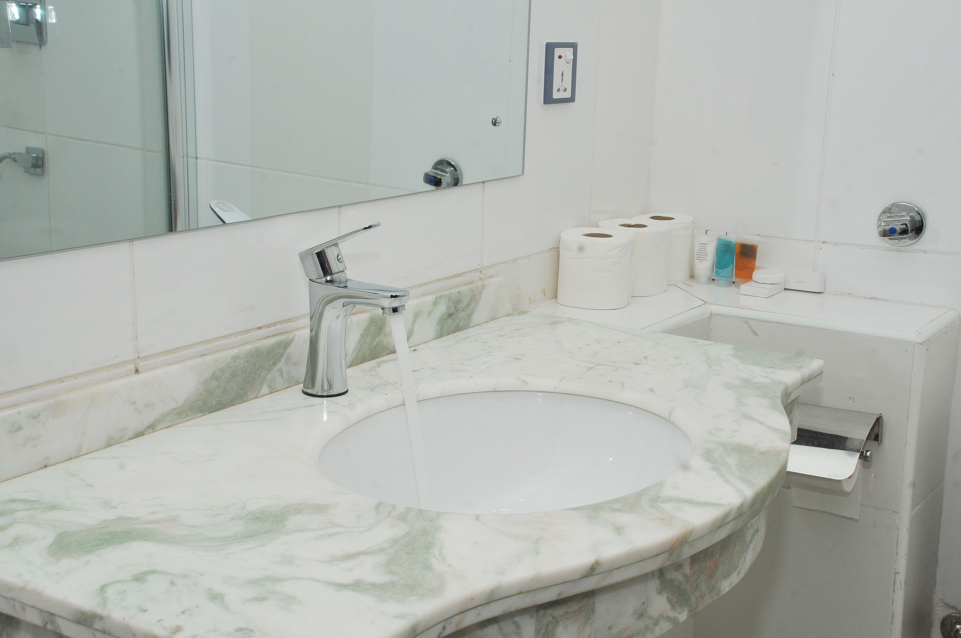 A bathroom with a marble sink, a mirror, and a toilet paper holder.
