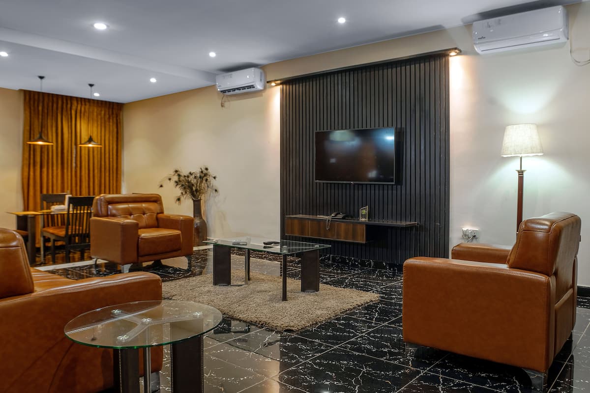 A modern living room with leather sofas, a glass coffee table, a flat-screen TV mounted on a dark wall, and a floor lamp.