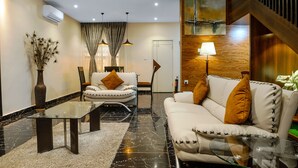 Una sala moderna con un sofá, sillones, una mesa de centro de vidrio y una lámpara.