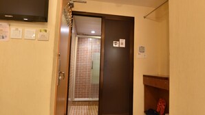 A hallway with a tiled floor, a door leading to a bathroom, a wall-mounted TV, and a shelf with slippers. - Wonderful Inn (Kowloon)