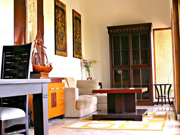 A well-lit living room with a sofa, coffee table, and a bookshelf labeled 'BIBLIOTHÈQUE'.